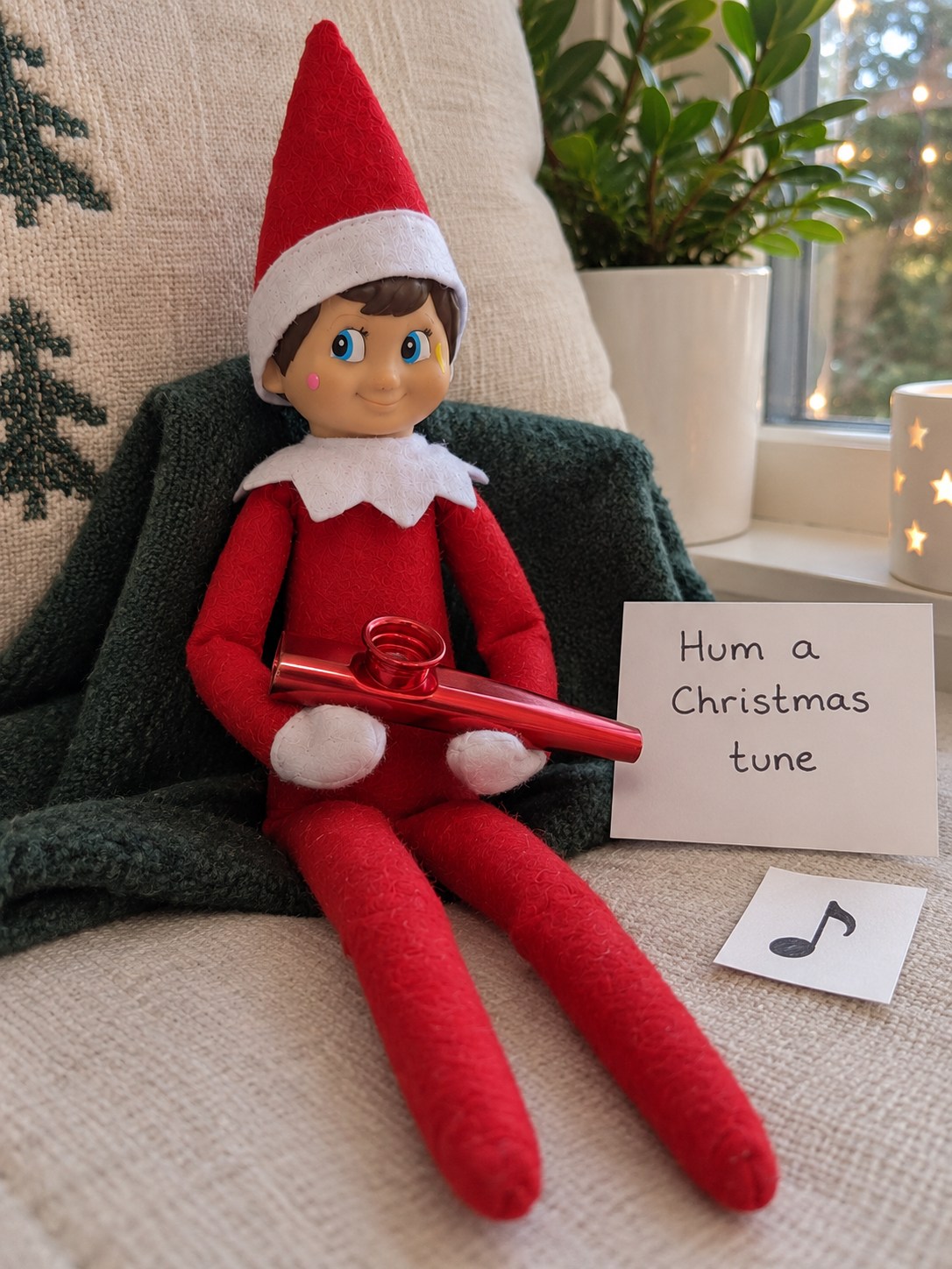 Tom's elf holding a red metal kazoo below his collar beside a Hum a Christmas tune note.