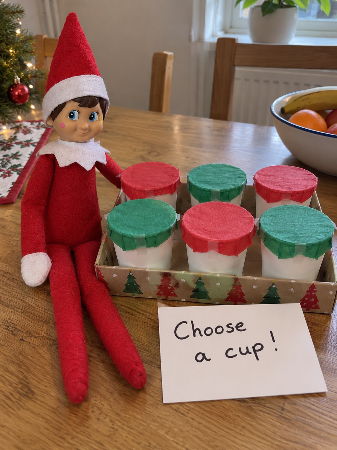 Tom's elf beside six paper cups with alternating red and green tissue covers and a Choose a cup note.