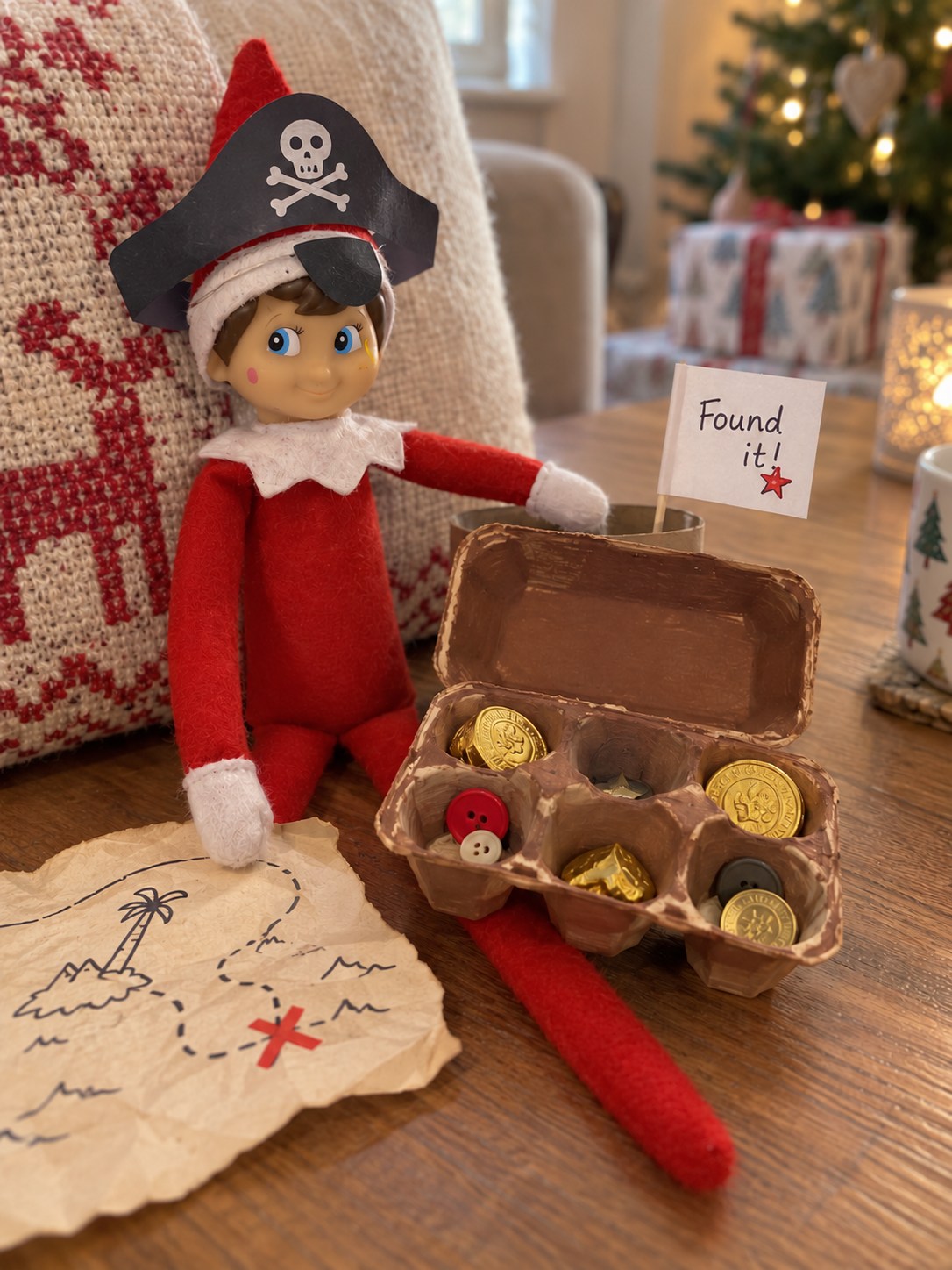 Tom’s elf wearing a folded paper pirate hat beside an open egg-box treasure chest containing buttons and wrapped chocolate coins.