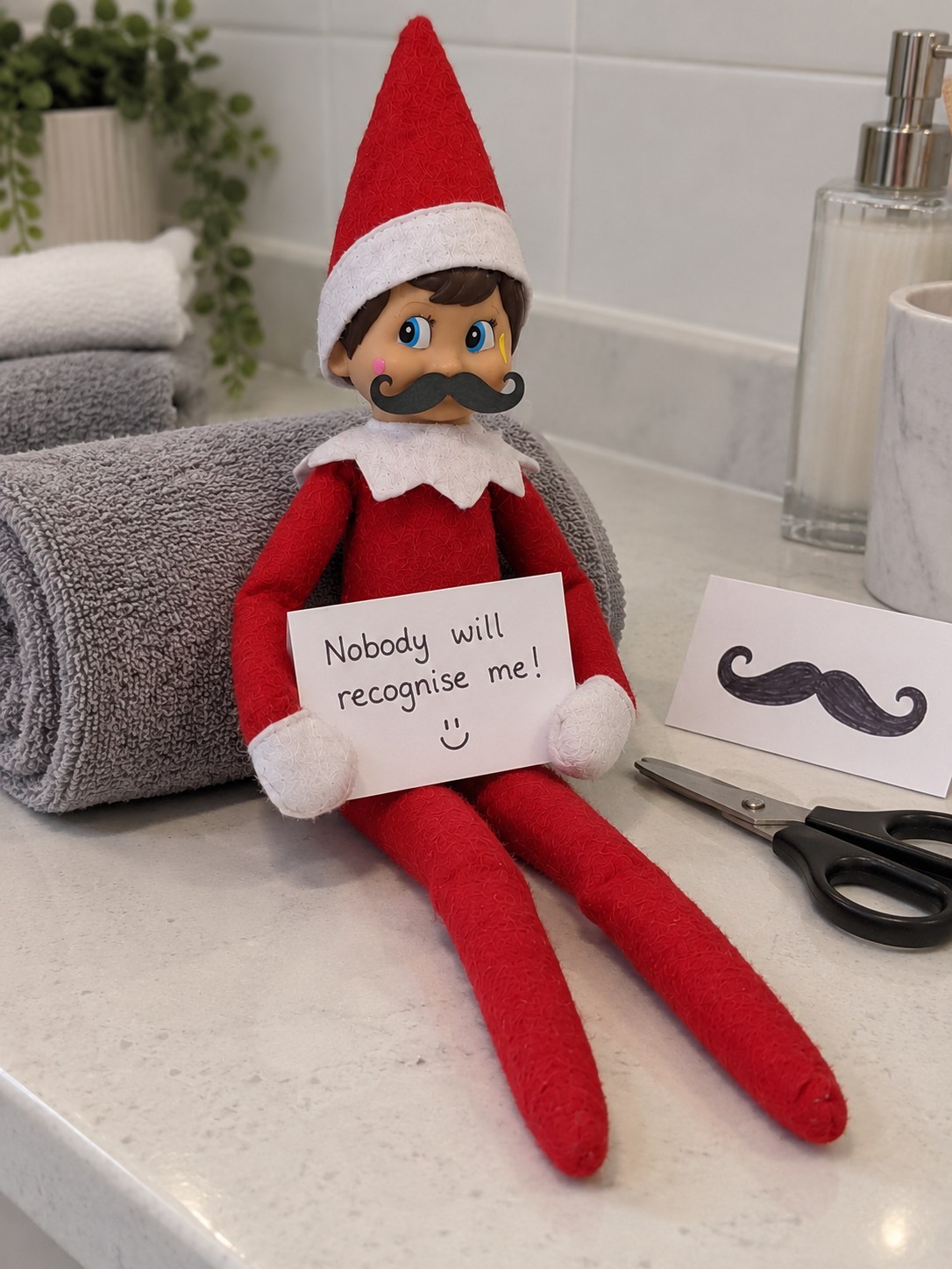 Tom’s elf wearing a curled black paper moustache beneath his nose and holding a Nobody will recognise me note.