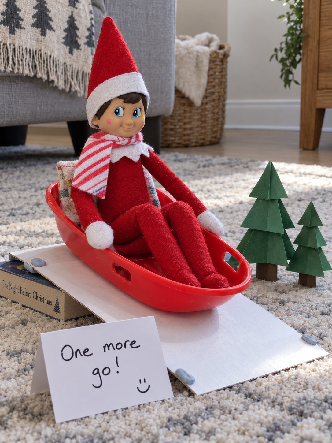 Tom’s elf seated in a shallow red sled with a red-and-white scarf on a low white cardboard slope beside a One more go note.