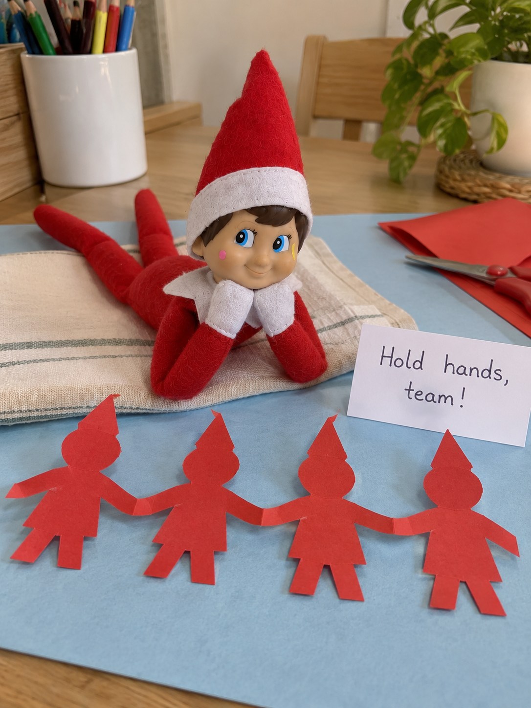 Tom's elf beside a handmade red accordion chain of four paper elf silhouettes holding hands.