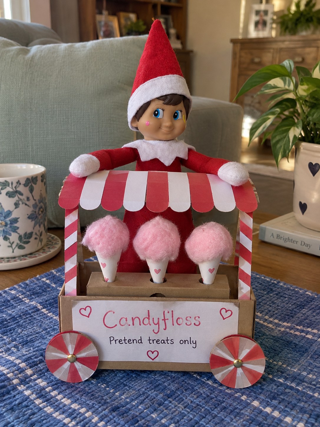 Tom’s elf behind a homemade cardboard candyfloss cart with a striped awning, three pink pretend candyfloss cones and a Pretend treats only note.