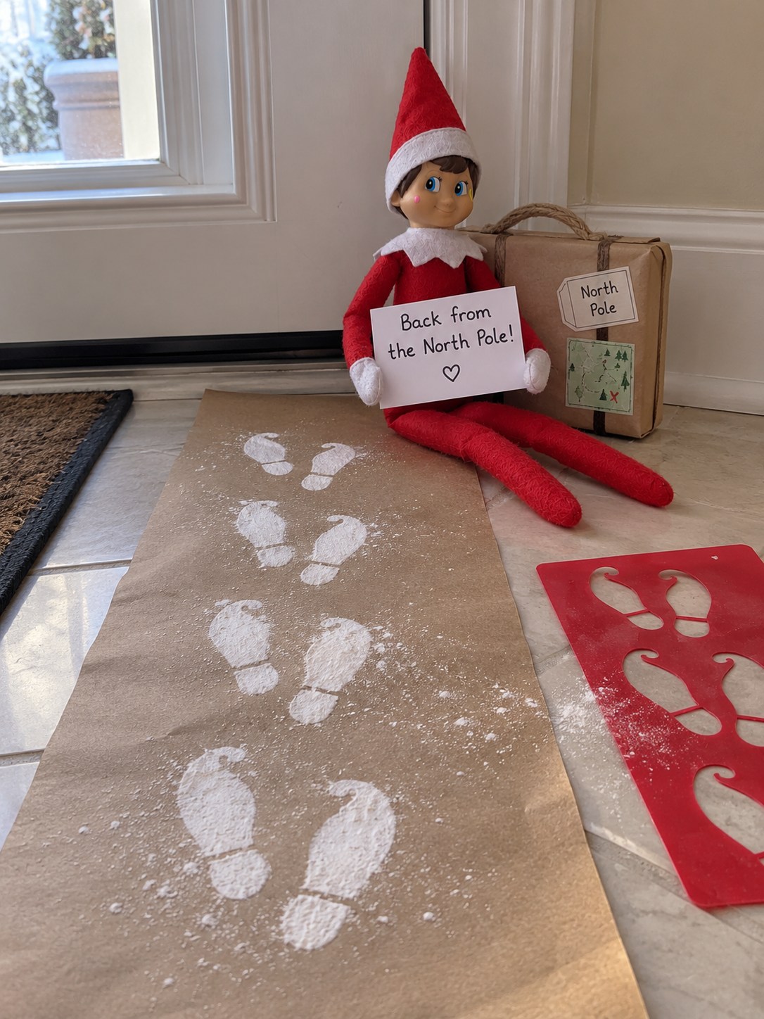 Tom’s elf beside a brown-paper trail of white curled-toe elf boot prints with red footprint stencils and a Back from the North Pole note.