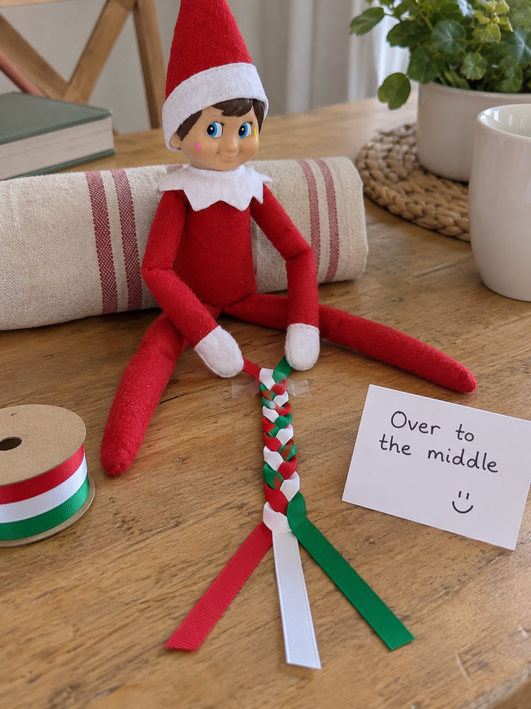 Tom's elf beside a three-strand red, green and white ribbon braid with three loose tails and an Over to the middle note.